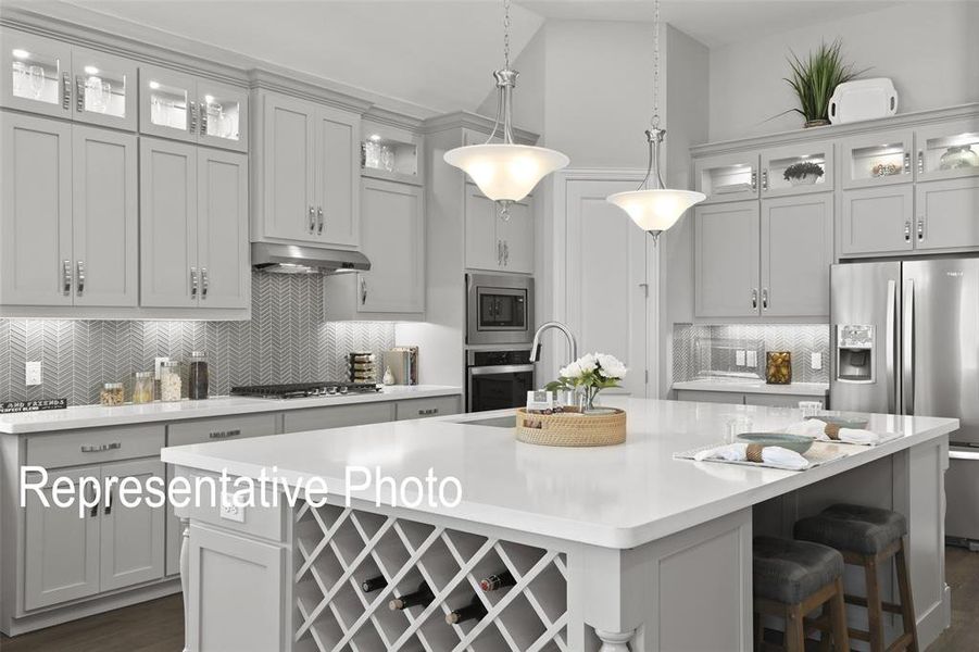 Kitchen featuring a large island with built-in wine storage, white countertops, gray cabinetry, stainless steel appliances, and a herringbone pattern tile backsplash Kitchen featuring a large island with built-in wine storage, white countertops, gray cabinetry, stainless steel appliances, and a herringbone pattern tile backsplash