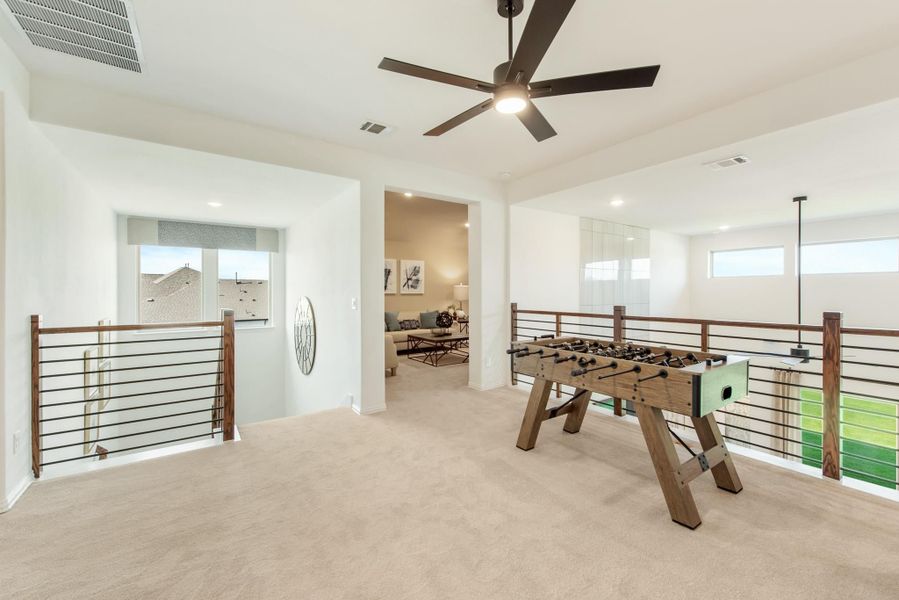Upstairs game room with foosball table, carpet flooring, ceiling fan, and open railing overlooking lower level Upstairs game room with foosball table, carpet flooring, ceiling fan, and open railing overlooking lower level