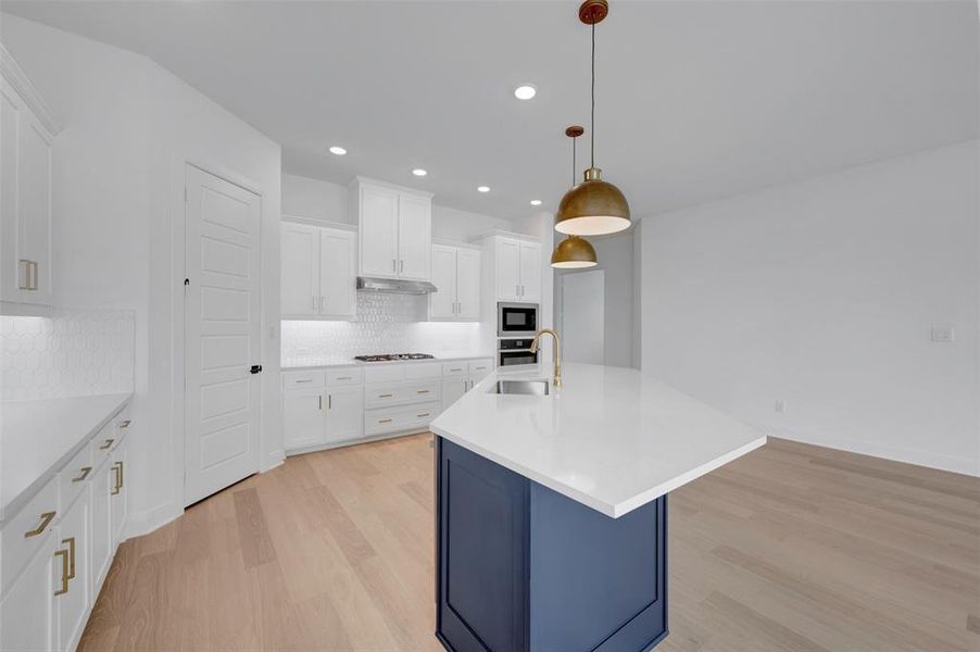 Dual tone kitchen with light wood-style floors, a kitchen island with sink, hanging light fixtures, light stone counters, and two tone cabinetry
