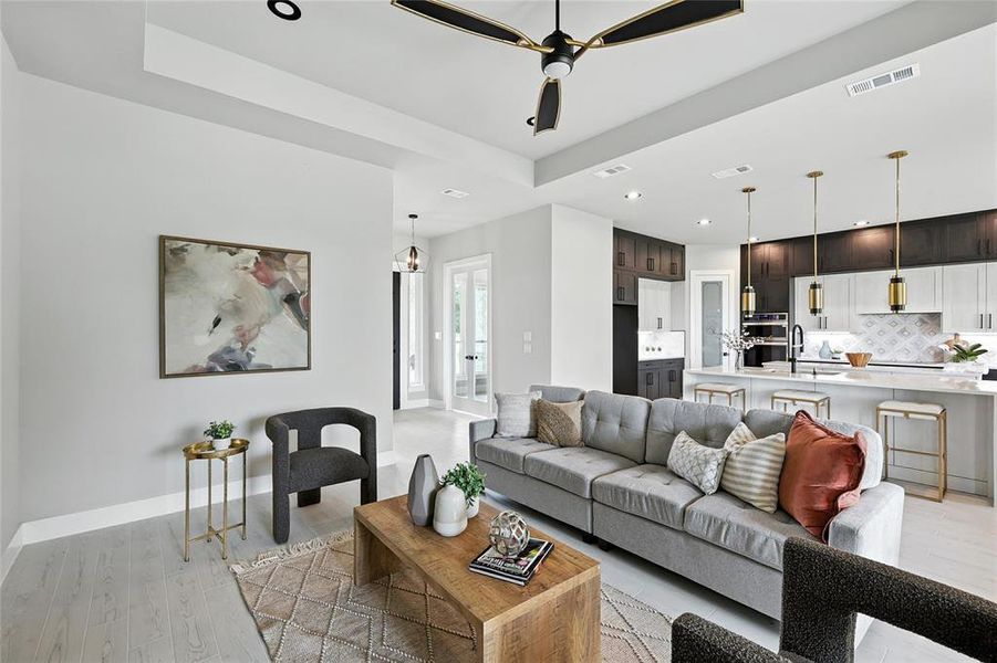 Living room with light wood-style floors, ceiling fan, recessed lighting, and a tray ceiling