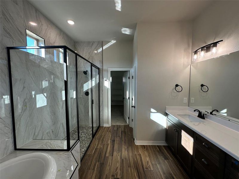 Full bath featuring vanity, a garden tub, a marble finish shower, a spacious closet, and dark wood-style floors Full bath featuring vanity, a garden tub, a marble finish shower, a spacious closet, and dark wood-style floors