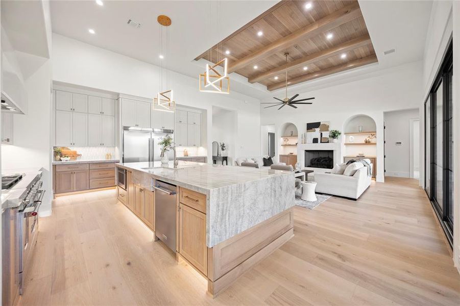 Kitchen featuring light brown cabinetry, light stone counters, a fireplace, a ceiling fan, and a wood ceiling with exposed beams