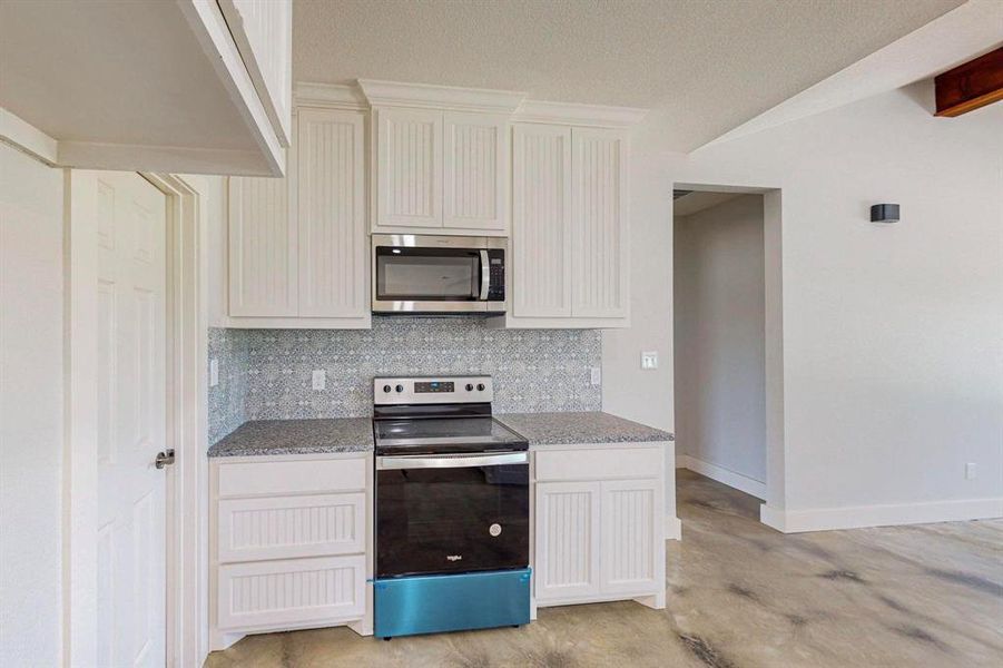 Kitchen featuring tasteful backsplash, white cabinetry, appliances with stainless steel finishes, and light stone counters