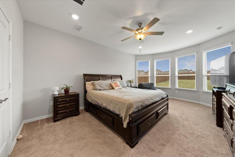 Primary bedroom with ceiling fan, and bay windows.