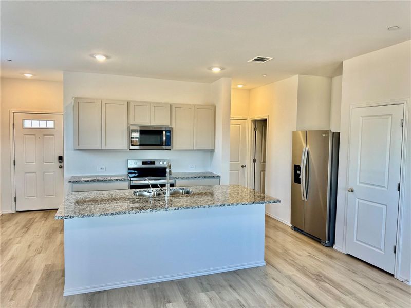 Kitchen featuring appliances with stainless steel finishes, light stone counters, light wood-style flooring, and a kitchen island with sink