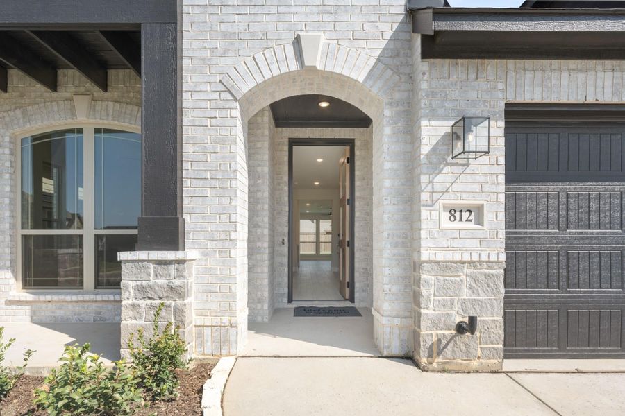 Home entrance with arched brick doorway, open front door, and dark garage door beside house number 812