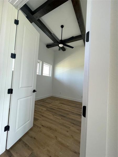 Empty room featuring wood finished floors, beam ceiling, and ceiling fan Empty room featuring wood finished floors, beam ceiling, and ceiling fan