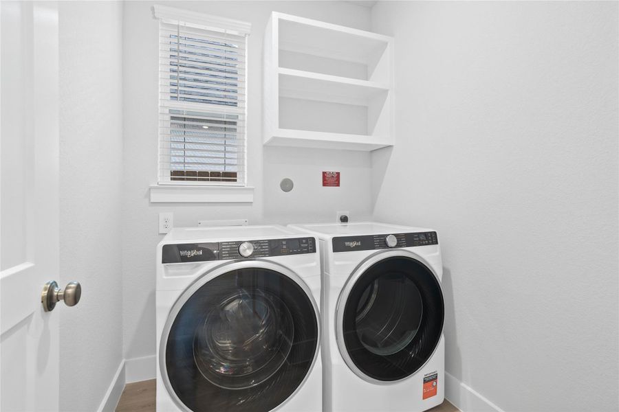 Convenient utility space showcasing Whirlpool front-load washer and dryer appliance set with shelving above to store your laundry needs. Convenient utility space showcasing Whirlpool front-load washer and dryer appliance set with shelving above to store your laundry needs.