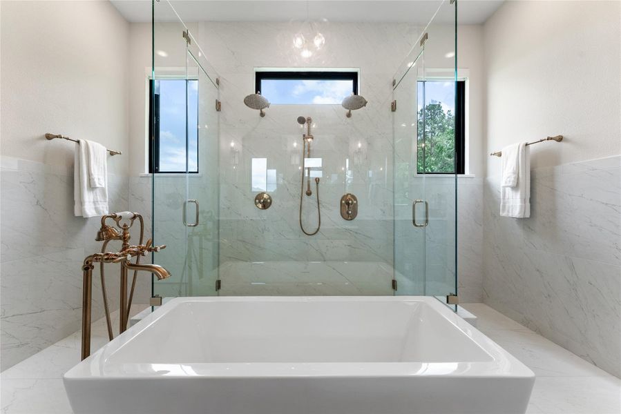 A standout shower design includes clear glass, specialty tile, multiple fixtures, and high windows for natural light. The result is a private spa-like space that feels custom and memorable.