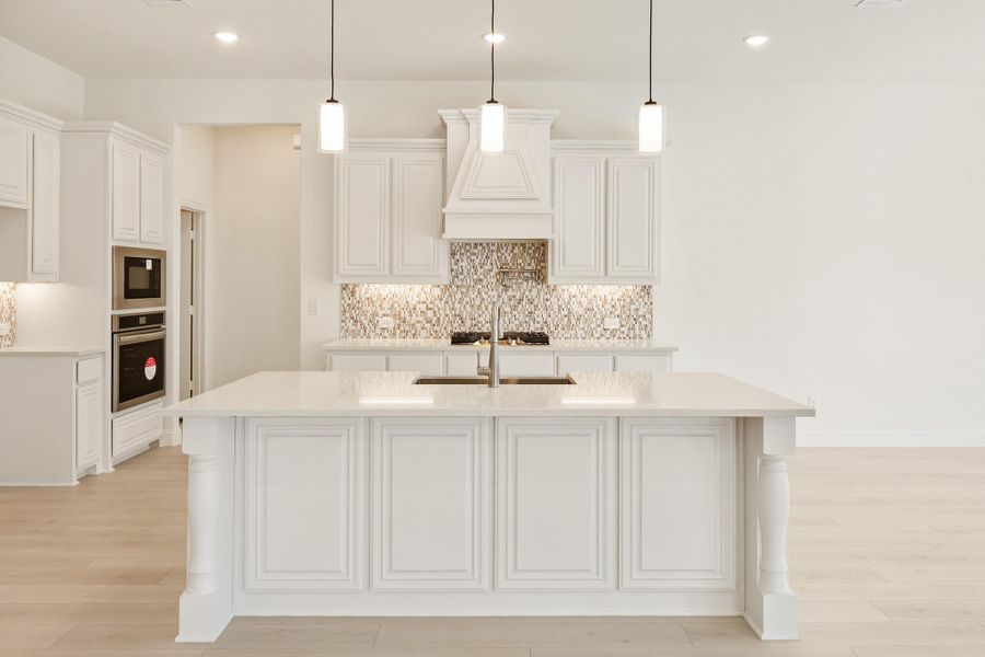 White kitchen with large island, pendant lights, mosaic tile backsplash, and stainless steel appliances White kitchen with large island, pendant lights, mosaic tile backsplash, and stainless steel appliances