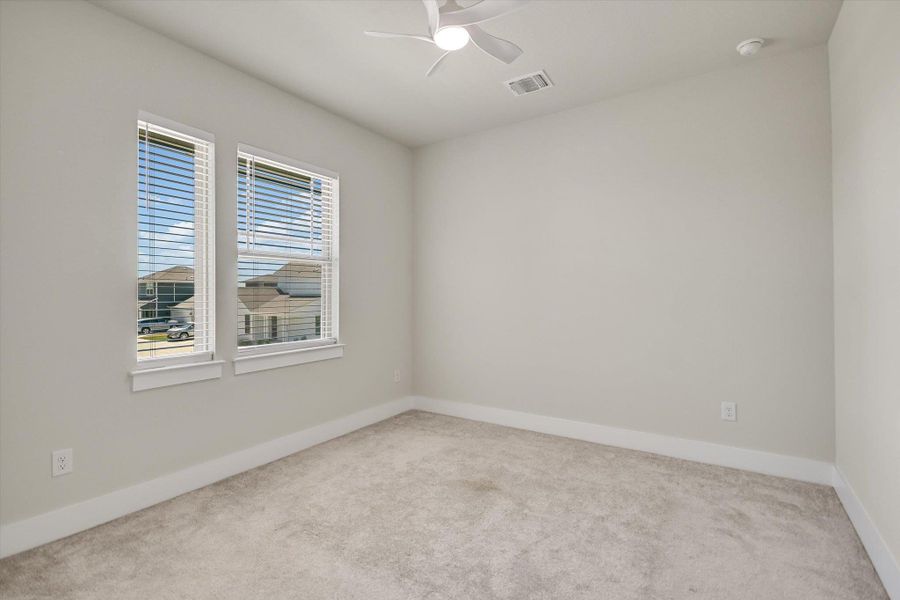 Double windows frame neighborhood views in a neutral bedroom finished with soft plush carpeting. Double windows frame neighborhood views in a neutral bedroom finished with soft plush carpeting.