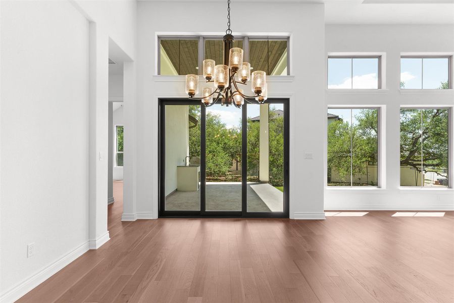 This spacious room features hardwood flooring, a large sliding glass door, and a decorative chandelier
