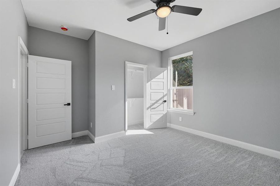 Unfurnished bedroom featuring light carpet, ceiling fan, and a walk in closet Unfurnished bedroom featuring light carpet, ceiling fan, and a walk in closet
