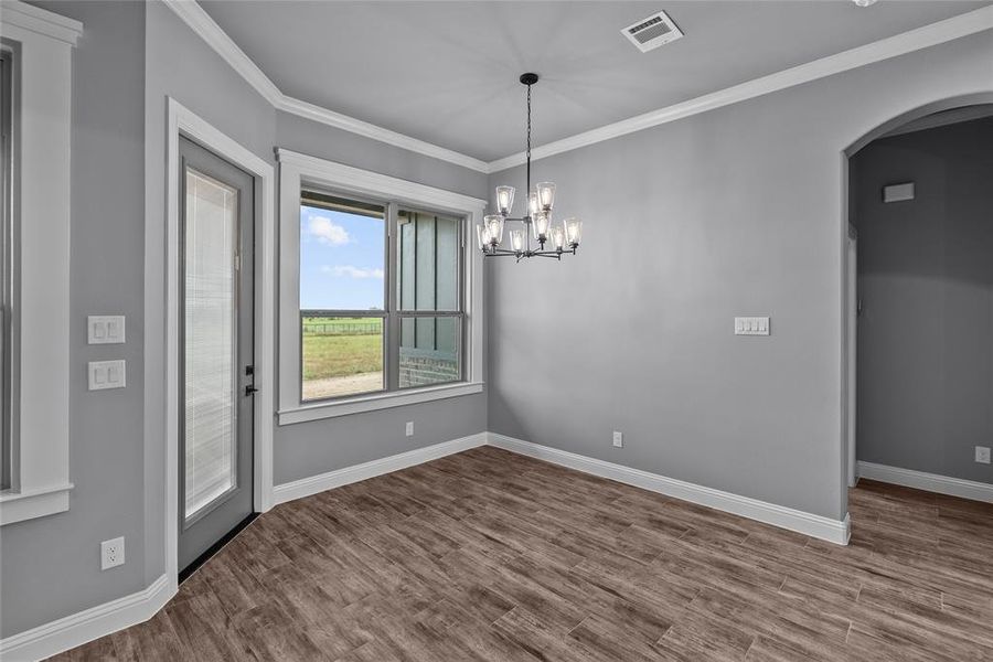 Unfurnished dining area featuring an inviting chandelier, crown molding, and hardwood / wood-style floors