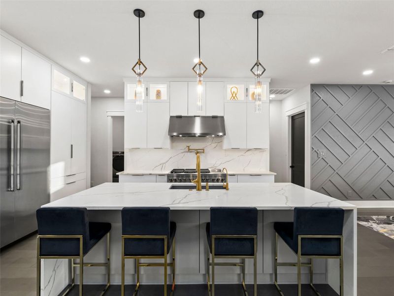 Kitchen featuring light stone counters, white cabinets, built in fridge, and hanging light fixtures