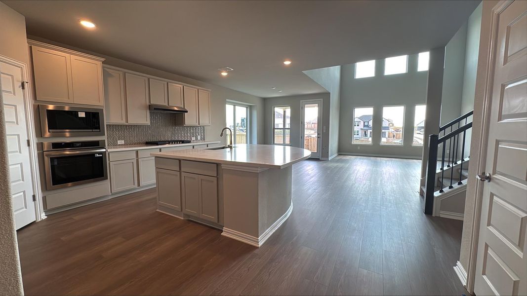 Kitchen featuring appliances with stainless steel finishes, backsplash, a kitchen island with sink, dark wood-style floors, and recessed lighting