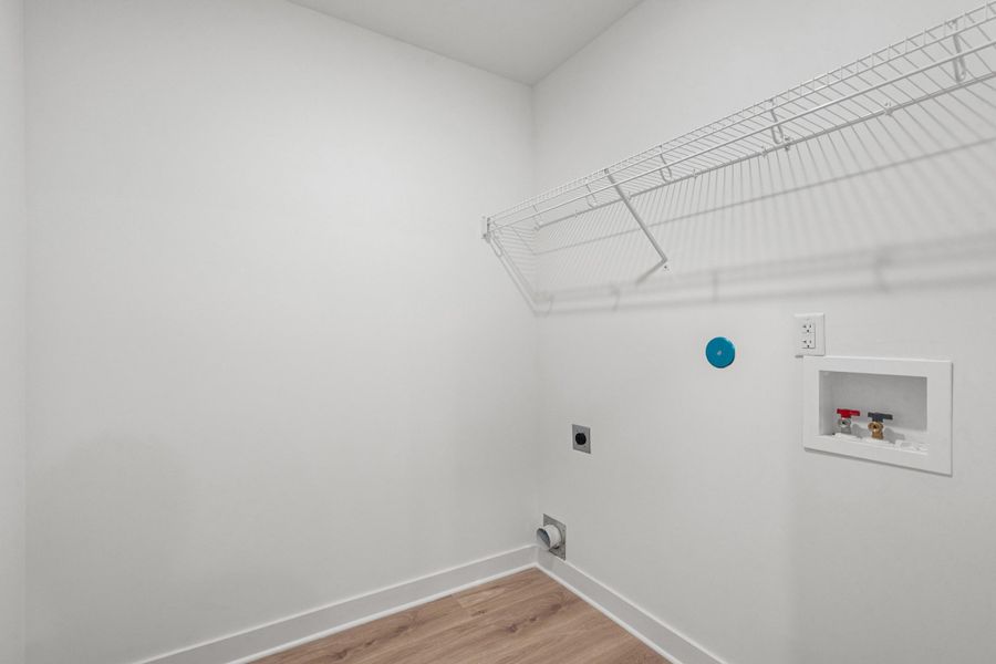 Dedicated laundry area featuring white wire shelving, wood-finish flooring, and crisp white walls