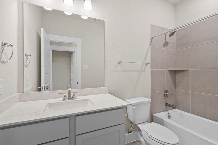 Image of a bathroom with grey cabinets, a mirror, and a shower and tub with tan tiles