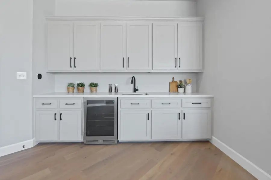 Indoor wet bar with beverage cooler and light wood-type flooring
