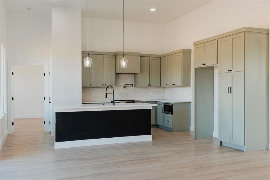 Kitchen with a high ceiling, pendant lighting, light wood-style flooring, a kitchen island with sink, and stainless steel microwave