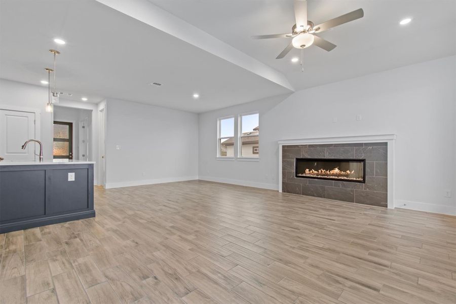 Unfurnished living room with ceiling fan, lofted ceiling, a fireplace, sink, and light hardwood / wood-style flooring