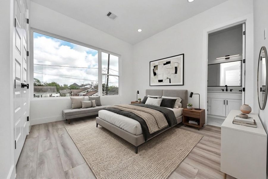 This bedroom features a modern design with large windows offering plenty of natural light. It includes a cozy bed, a stylish sitting area, and an en-suite bathroom. The neutral color palette and sleek furnishings create a calming and inviting atmosphere.