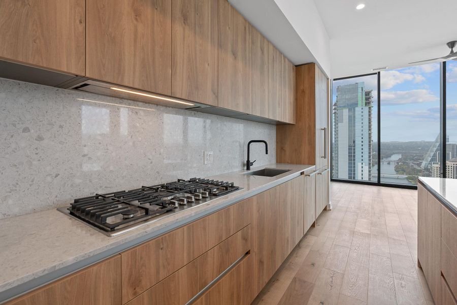 Kitchen with modern cabinets, a wall of windows, light stone countertops, light wood-type flooring, and backsplash