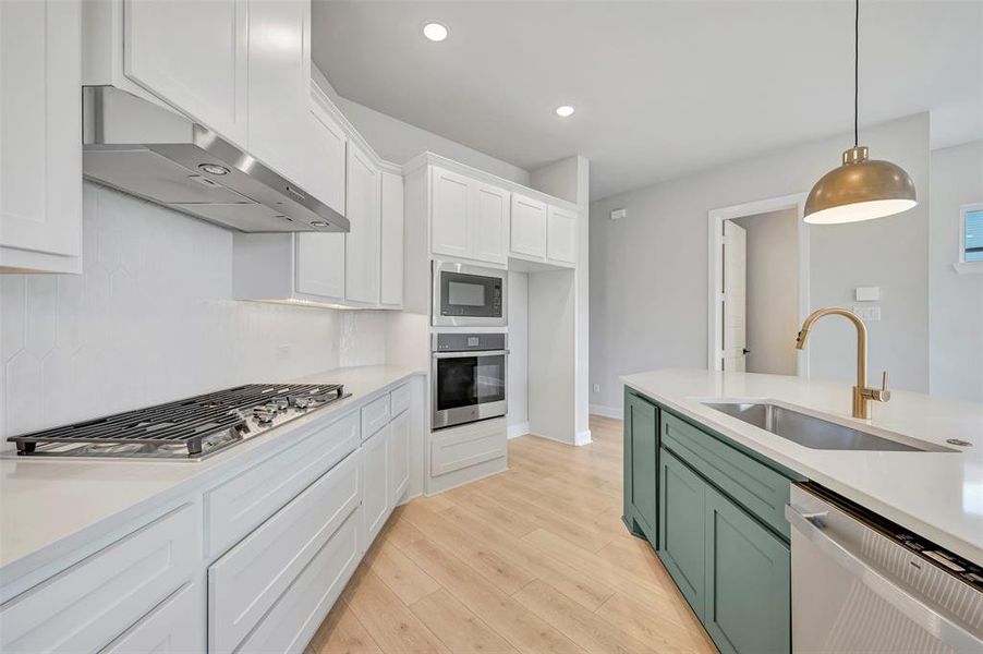 Two tone kitchen featuring two tone color scheme, stainless steel appliances, light wood-style floors, light stone countertops, and hanging light fixtures Two tone kitchen featuring two tone color scheme, stainless steel appliances, light wood-style floors, light stone countertops, and hanging light fixtures