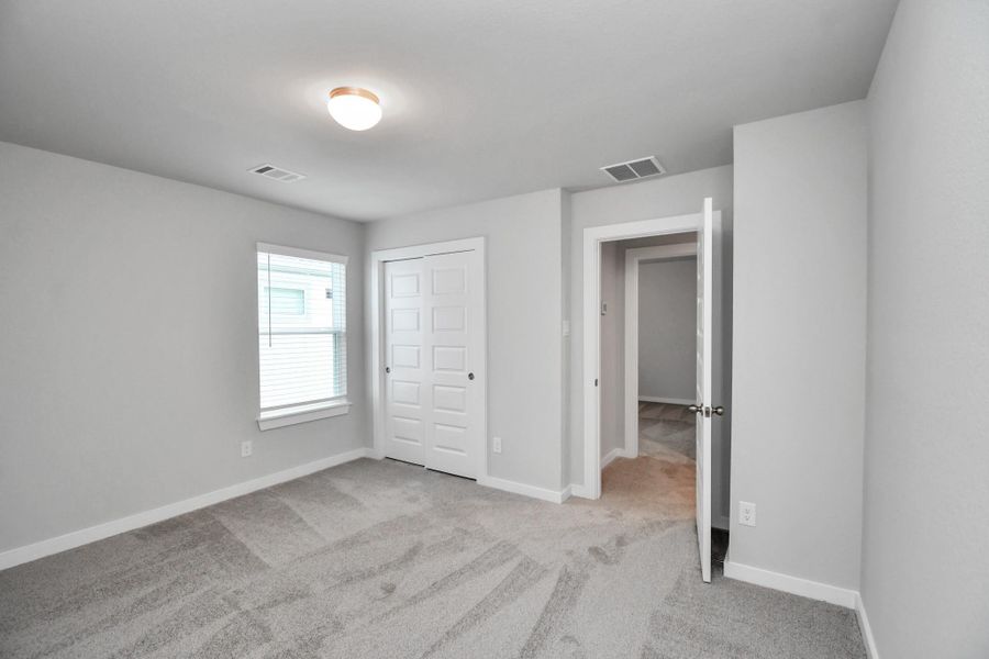 Secondary bedroom features plush carpeting, large windows that let in plenty of natural light, bright paint, and spacious closets. Sample photo of completed home with similar floor plan. Actual colors and selections may vary.