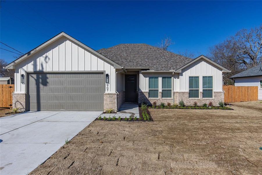 View of front of home with brick siding, board and batten siding, an attached garage, and fence