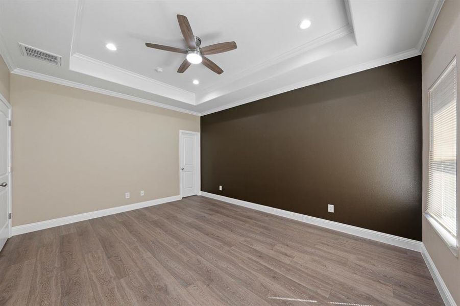 Empty room with a tray ceiling, crown molding, visible vents, wood finished floors, and baseboards