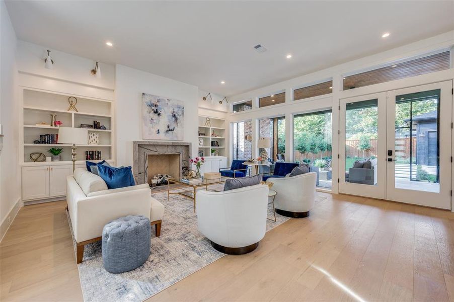 Living room with french doors, built in features, light hardwood / wood-style floors, and a high end fireplace