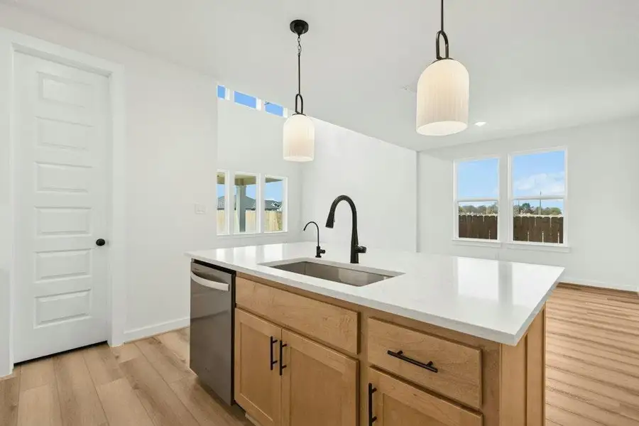 Kitchen with light brown cabinetry, pendant lighting, light wood finished floors, dishwasher, and light stone countertops