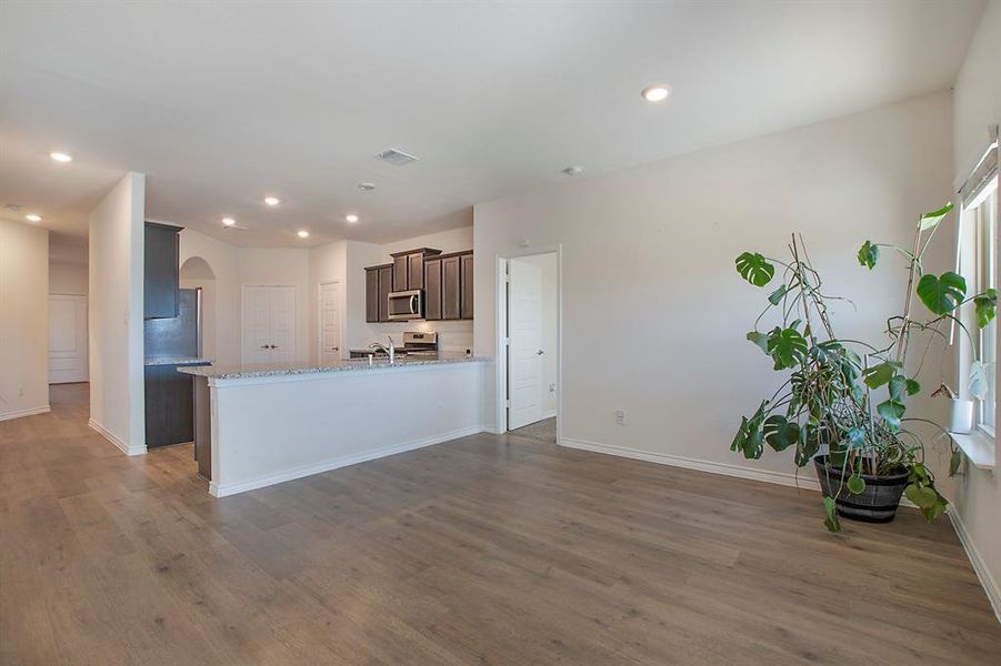 Kitchen featuring dark wood-type flooring, kitchen peninsula, stainless steel appliances, sink, and light stone counters