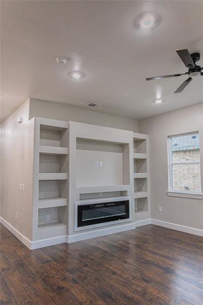 Unfurnished living room featuring built in features, a glass covered fireplace, dark wood-style floors, and recessed lighting Unfurnished living room featuring built in features, a glass covered fireplace, dark wood-style floors, and recessed lighting