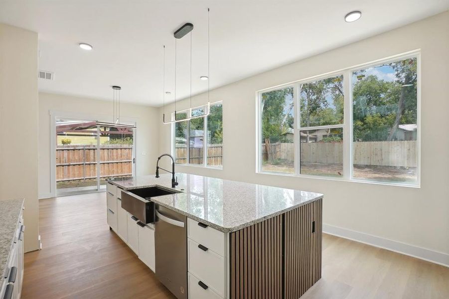 Kitchen featuring an island with sink, hanging light fixtures, sink, white cabinetry, and light hardwood / wood-style floors