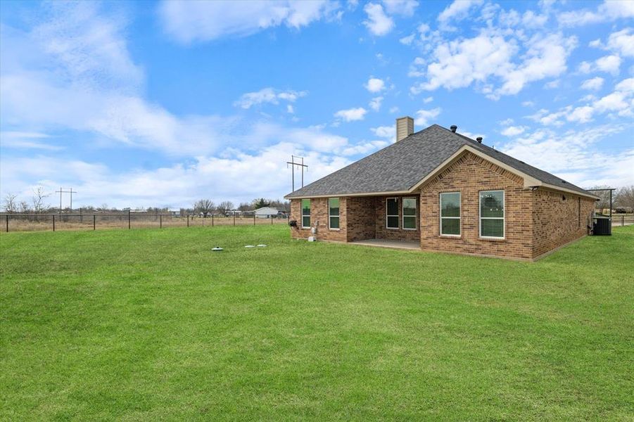 Rear view of house featuring roof with shingles, brick siding, a yard, a chimney, and fence