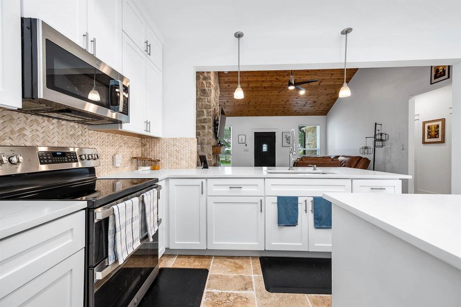 This beautifully appointed kitchen features sleek white cabinetry, stainless steel appliances, and a spacious island designed for both everyday living and entertaining. Stylish lighting, warm wood accents, and the open flow into the living area create a welcoming and functional gathering space.