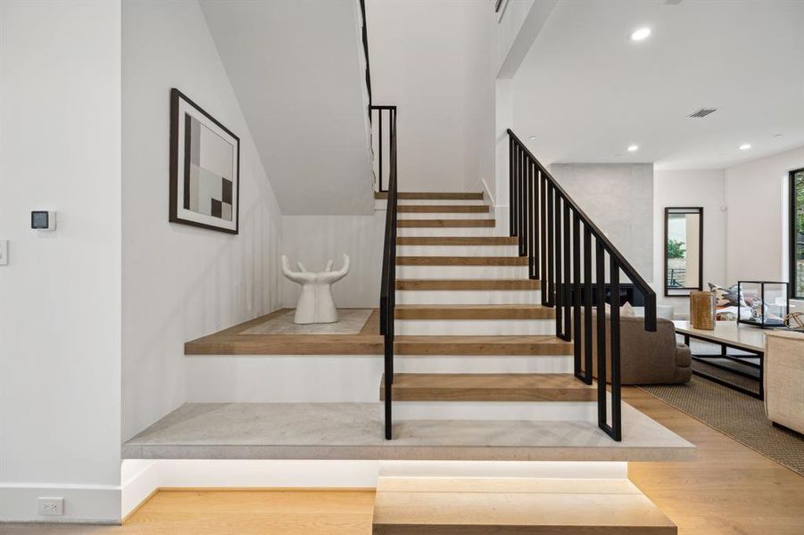 The stairs feature wide, light-toned wooden steps contrasted by sleek black metal railings while the open riser design creates an airy and spacious feel.