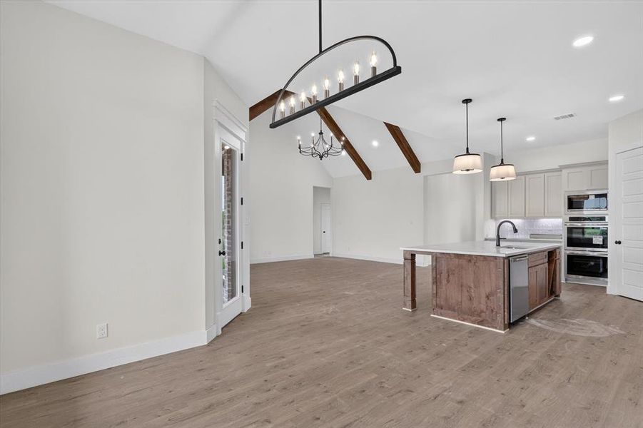 Open-concept living space featuring wood-finish flooring, vaulted ceilings with exposed beams, and contemporary lighting Open-concept living space featuring wood-finish flooring, vaulted ceilings with exposed beams, and contemporary lighting
