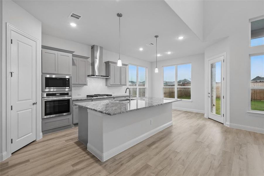 Kitchen with appliances with stainless steel finishes, gray cabinets, wall chimney exhaust hood, light stone countertops, and recessed lighting
