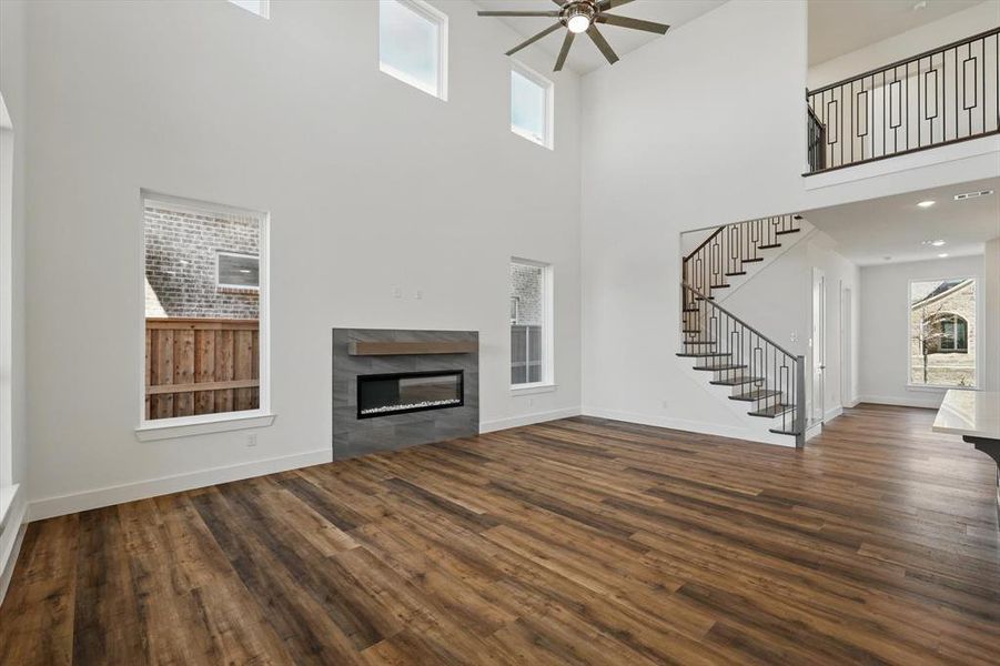 Unfurnished living room featuring stairs, baseboards, dark wood finished floors, and a tiled fireplace