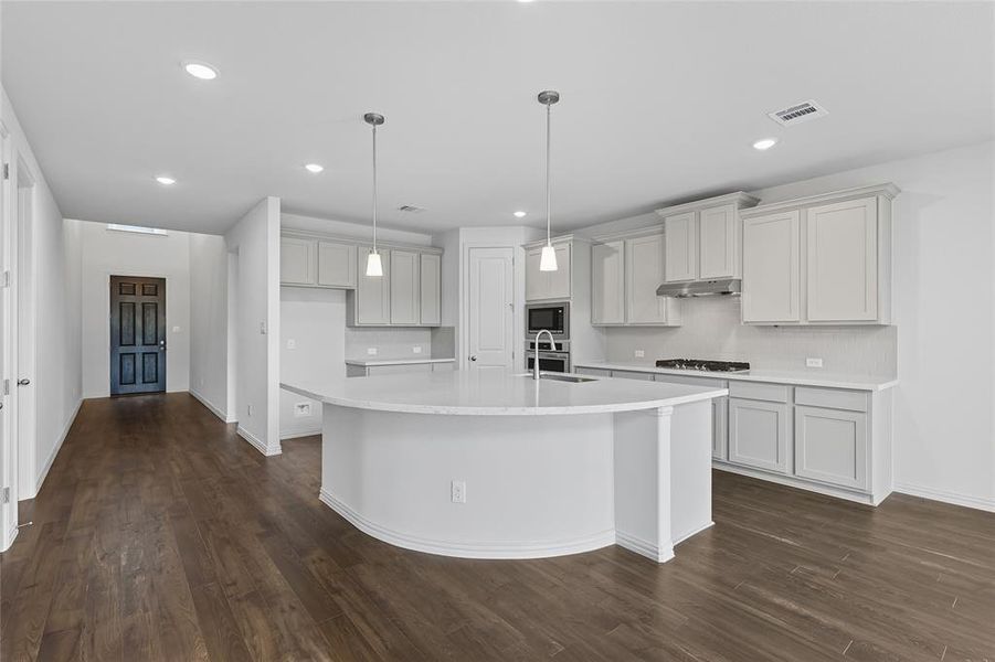 Kitchen with a kitchen island with sink, dark wood-style flooring, tasteful backsplash, and light stone countertops Kitchen with a kitchen island with sink, dark wood-style flooring, tasteful backsplash, and light stone countertops