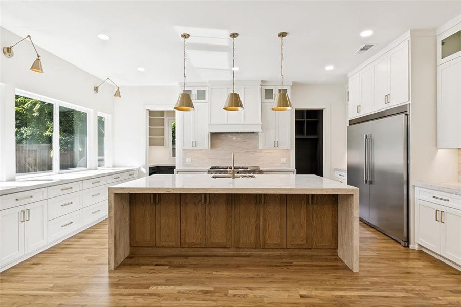 Kitchen featuring a waterfall island with wood-finish cabinetry, stainless steel appliances, recessed lighting, brass-toned pendant lights, and a window seat with built-in storage Kitchen featuring a waterfall island with wood-finish cabinetry, stainless steel appliances, recessed lighting, brass-toned pendant lights, and a window seat with built-in storage