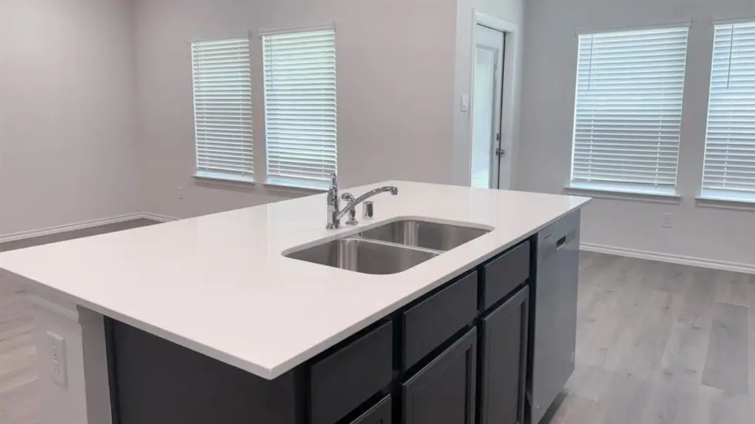 Kitchen featuring an island with sink, dark cabinets, light wood-type flooring, dishwasher, and light stone counters