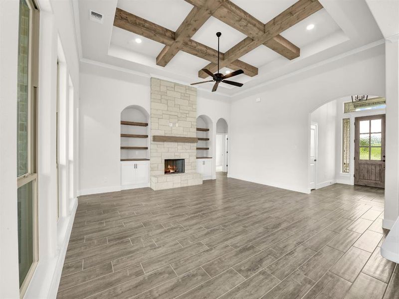 Unfurnished living room featuring wood finish floors, coffered ceiling, beam ceiling, a fireplace, and ceiling fan