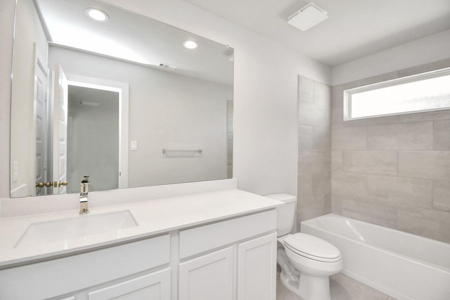 Secondary bath features tile flooring, bath/shower combo with tile surround, light stained wood cabinets, beautiful light countertop. Sample photo of completed home with similar floor plan. Actual colors and selections may vary.