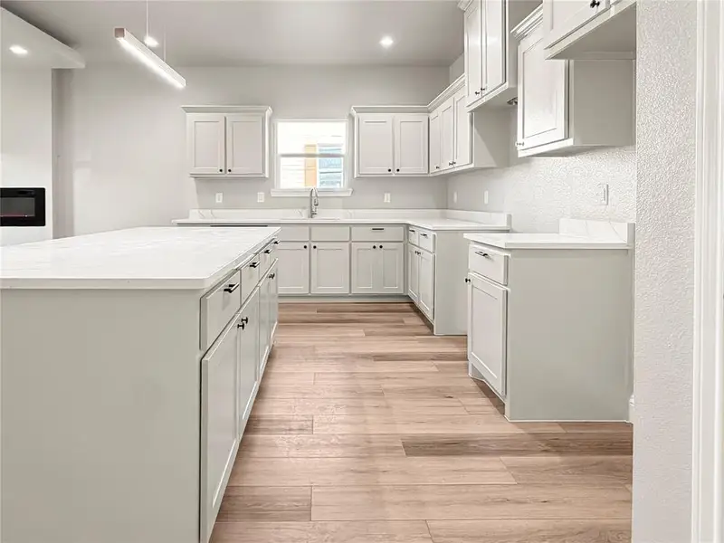 Spacious kitchen featuring a large island, extensive white cabinetry, light countertops, wood-finish flooring, and a built-in oven