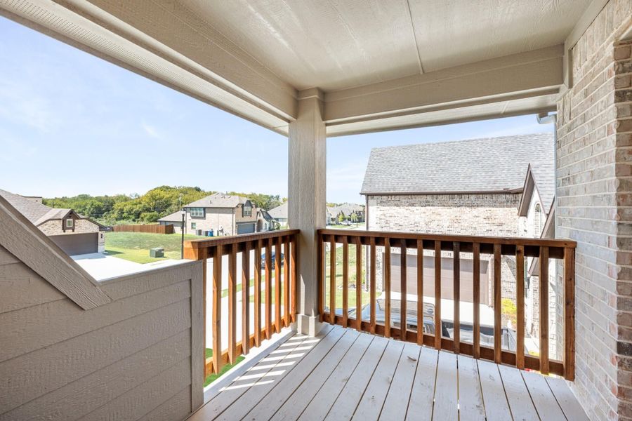 Covered second-floor balcony with wood railing and views of neighboring brick homes and green hills Covered second-floor balcony with wood railing and views of neighboring brick homes and green hills