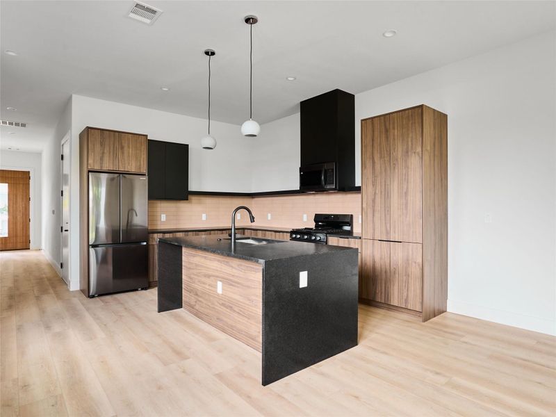 Kitchen with modern cabinets, appliances with stainless steel finishes, dark stone counters, a kitchen island with sink, and light wood-style flooring Kitchen with modern cabinets, appliances with stainless steel finishes, dark stone counters, a kitchen island with sink, and light wood-style flooring